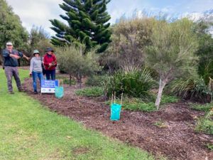Three people stand near a garden area with a sign reading 