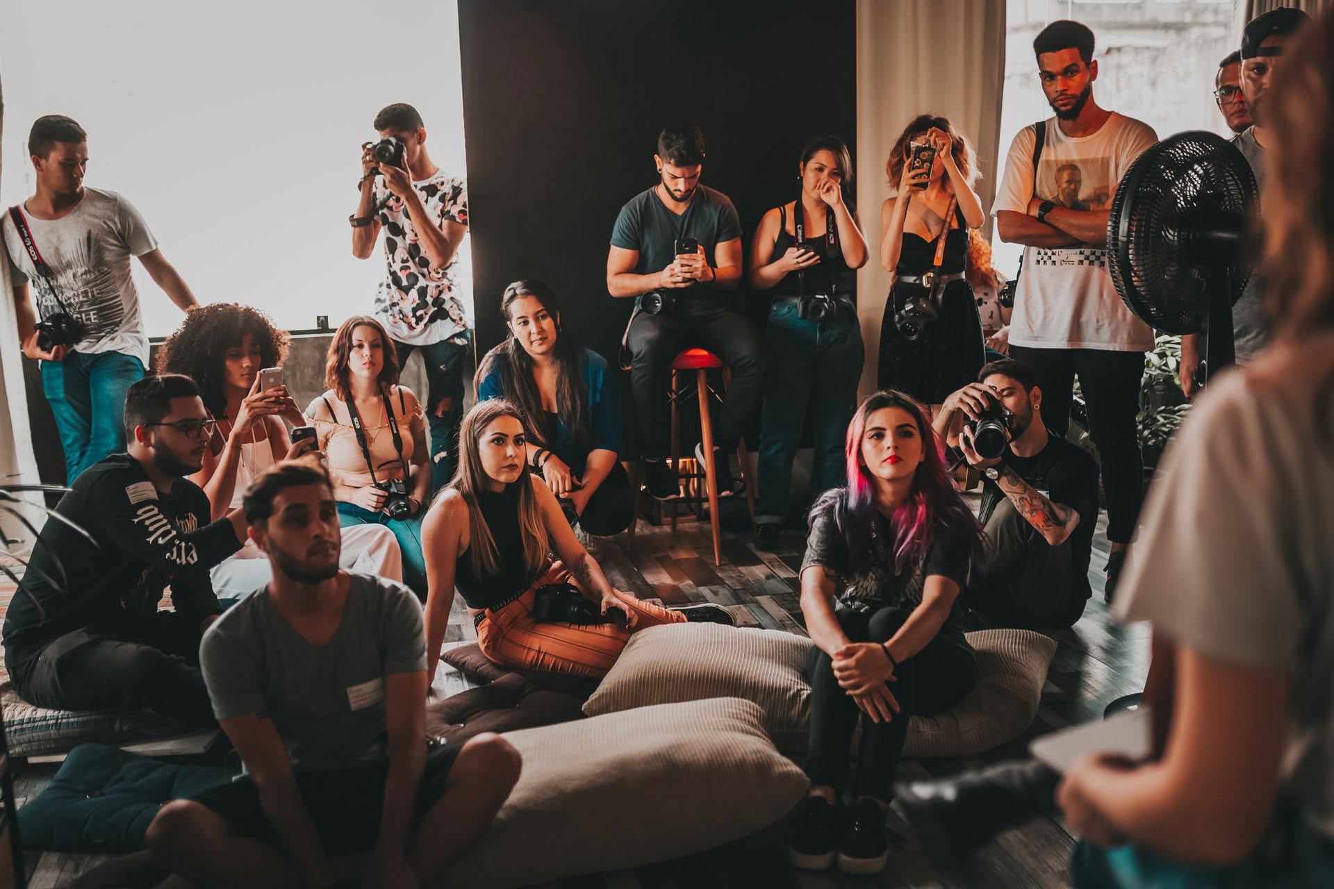 Members of the Augusta Community Development Association gathered indoors, some seated on cushions and others standing, attentively listening and taking photos.